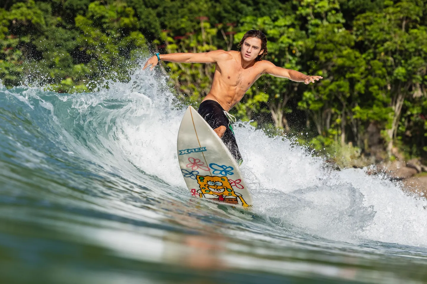 Andre Mei surfando uma onda no litoral norte de São Paulo, com mata verde ao fundo